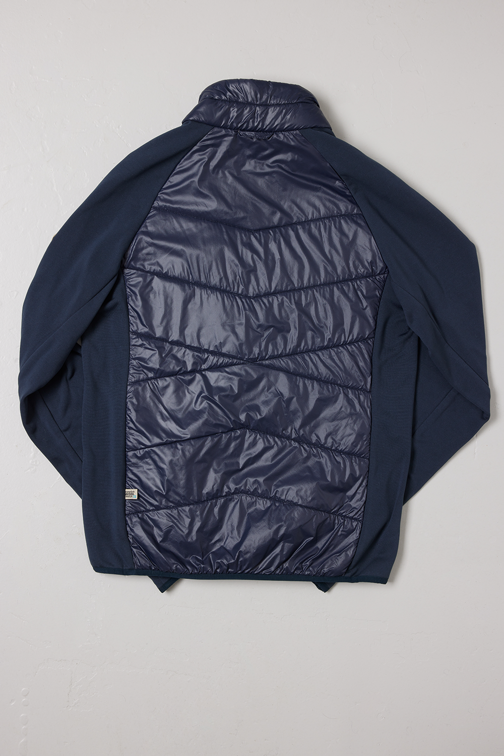 Baksidan av en blå-färgad SUFFOLK Hybrid jacka, herrmodell, från Wool Rebel, fotograferad mot en vit bakgrund.