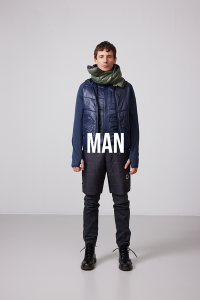 En man står iklädd en SUFFOLK Hybrid jacka från Wool Rebel, fodrad med FÅRTEX. Jackan har en mörkblå färg. 