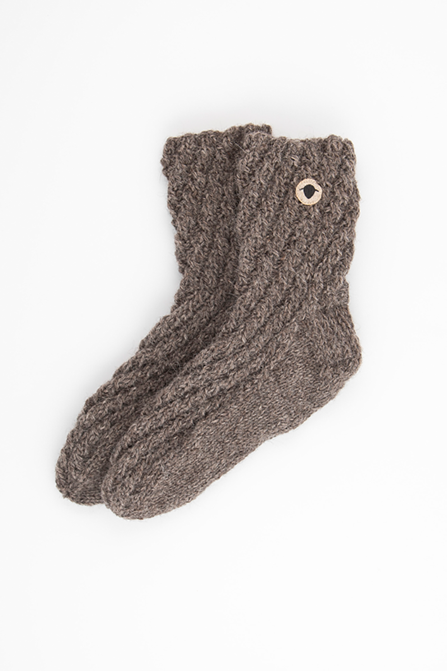 Ett par handstickade SHETLAND-sockar från Wool Rebel placerade på en ljus bakgrund. Wool Rebel-logotypen vid sockans skaft.